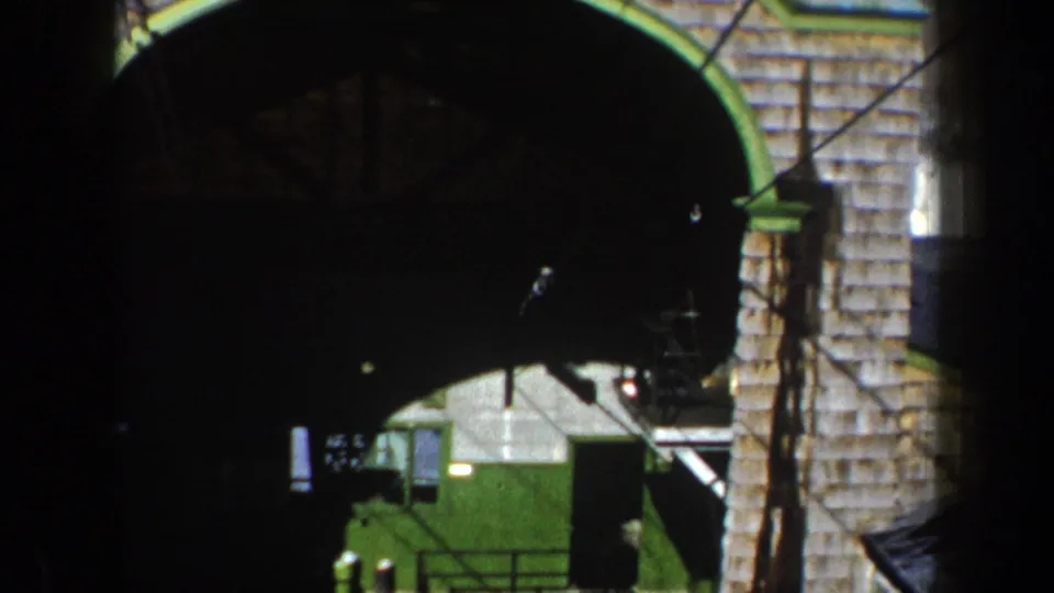 New York archival home-movie frame showing the cableway station area beneath a stone archway and overhead cables.