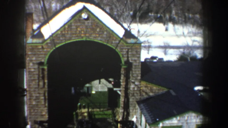 1962 New York home-movie still showing the stone arch, green trim, snow, and a nearby small white building.