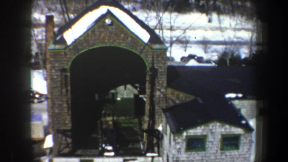 1962 New York frame with the arched stone structure offset beside a small white building and snowy ground.
