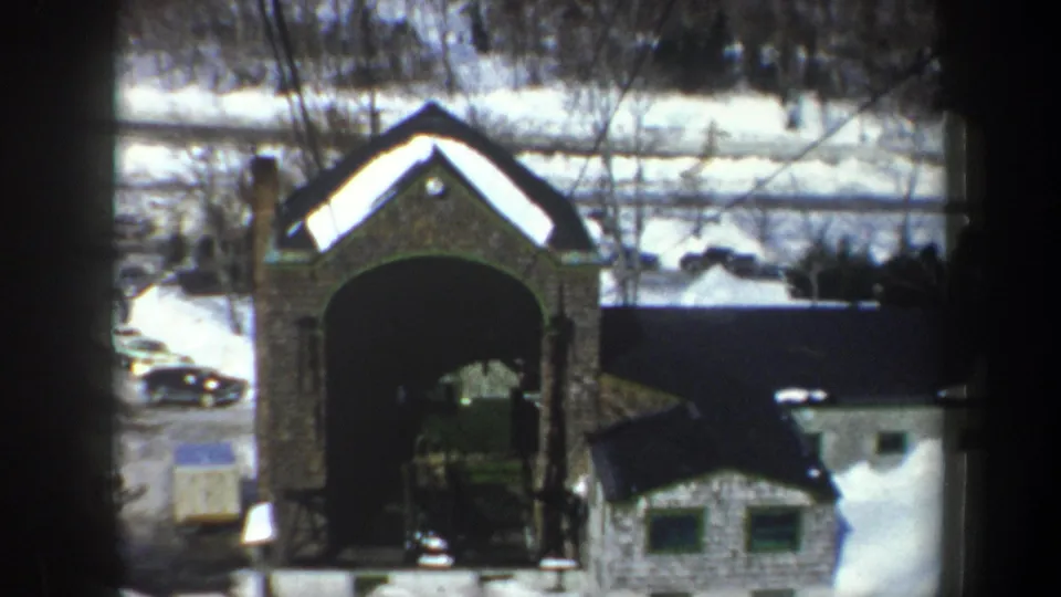 Elevated 1962 New York view of a stone archway, snow-covered small building, roadside area, and winter trees.