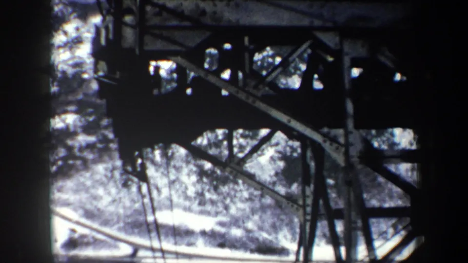 1962 New York 8mm frame with utility structure, cables, snow-covered hillside, and dark vignette from the film frame.