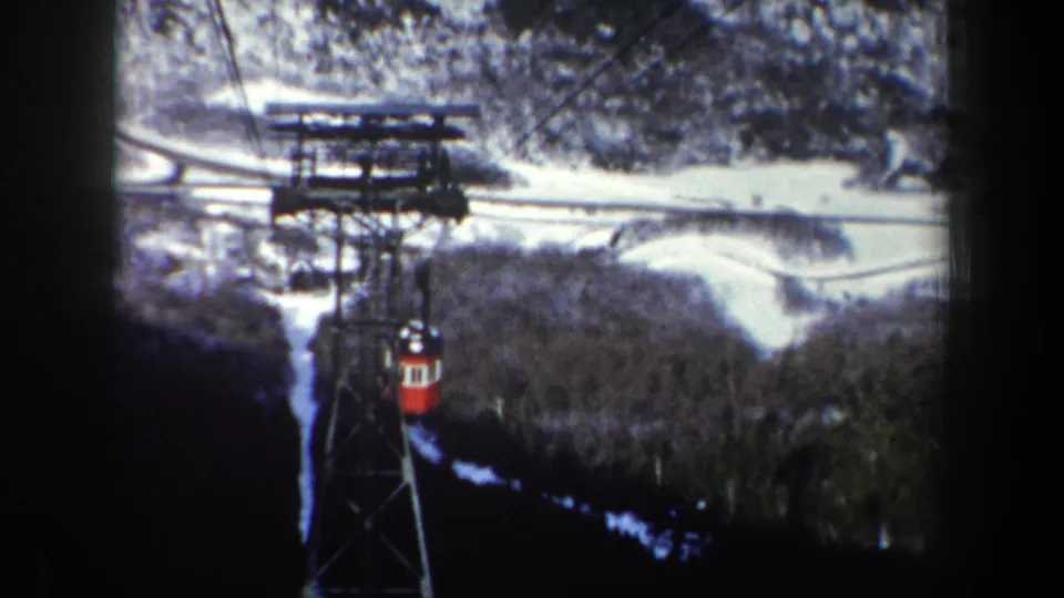 1962 New York home-movie view of a red aerial tram moving along cables above snow patches and winter woods.