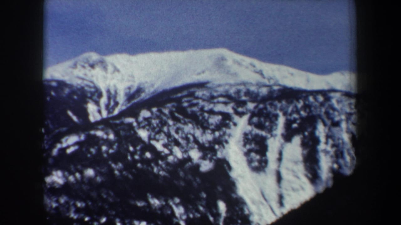 1962 New York 8mm frame showing a snowy mountain ridge, rocky dark slope, and clear blue sky within visible film edges.