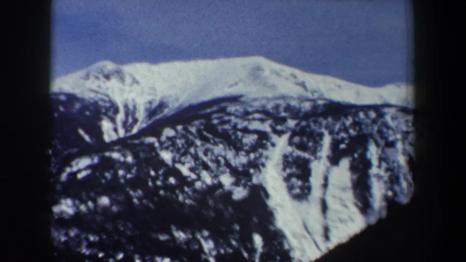 1962 New York 8mm frame showing a snowy mountain ridge, rocky dark slope, and clear blue sky within visible film edges.