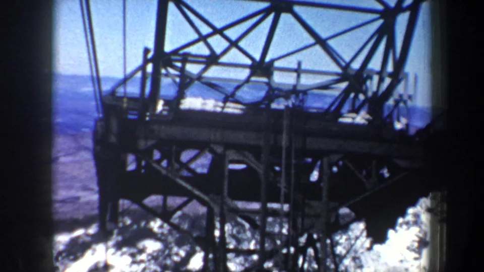 1962 New York 8mm frame showing a large metal tower structure in front of distant snowy mountains and blue sky.