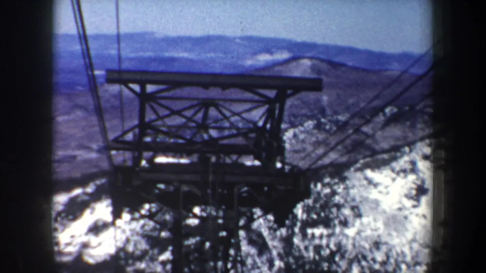 A vintage 8mm view of a cable car or ski lift tower above snow-covered New York mountain terrain in 1962.