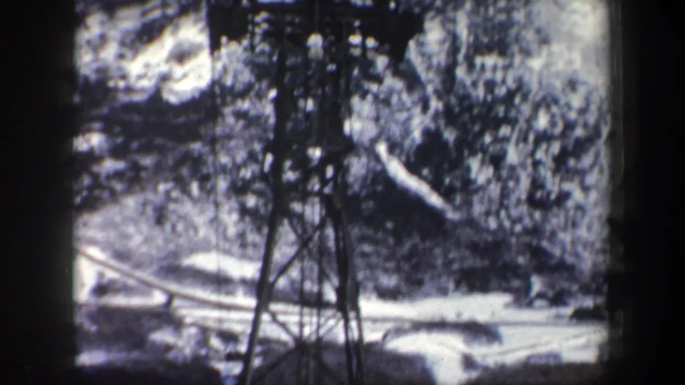 The camera looks past the lower lift tower structure toward snow-covered ground and a pale winding road or track below.