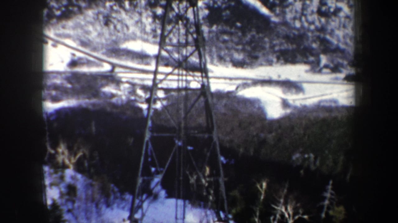 1962 New York 8mm frame showing a power transmission tower above snow-covered trees and winding ski terrain.