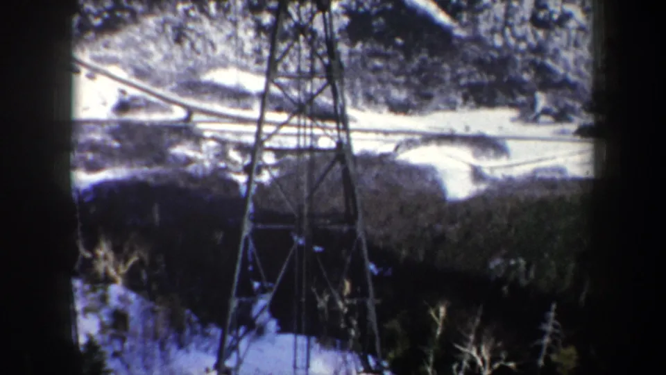 1962 New York 8mm frame showing a power transmission tower above snow-covered trees and winding ski terrain.