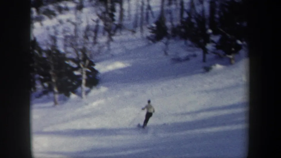 1962 New York 8mm frame showing a lone skier crossing a broad groomed slope with woods along the upper edge.