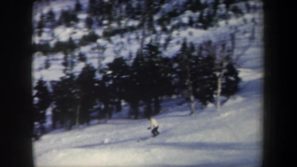 1962 New York 8mm frame with a skier near the bottom of a snowy run bordered by evergreen trees.