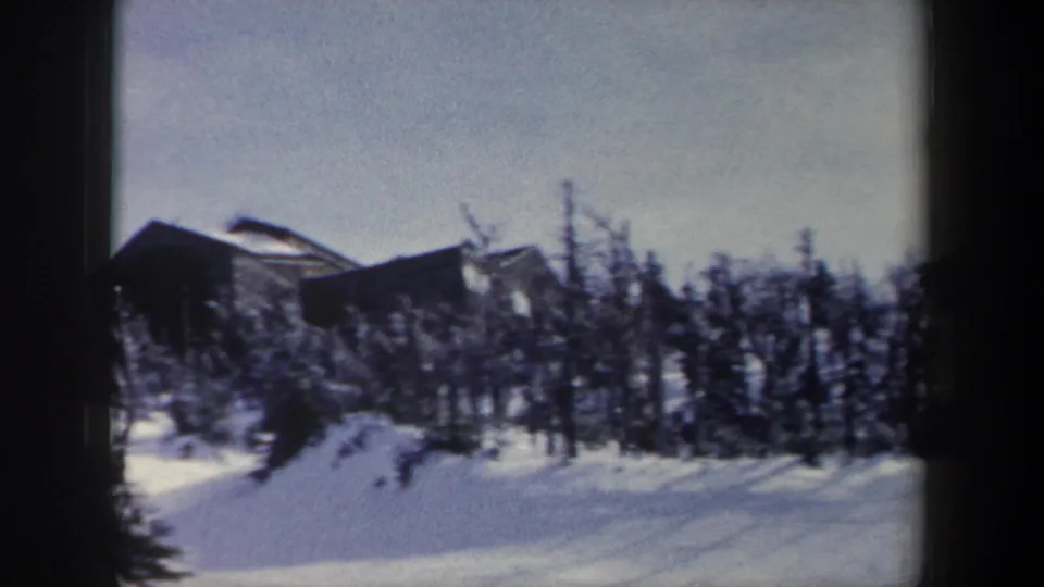 1962 New York 8mm frame showing a dark cabin beyond winter trees and deep snow in the foreground.