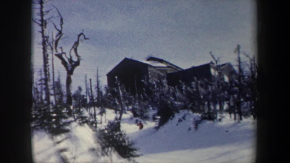 1962 New York 8mm frame showing a cabin among winter trees and a distant red-coated figure crossing snow.