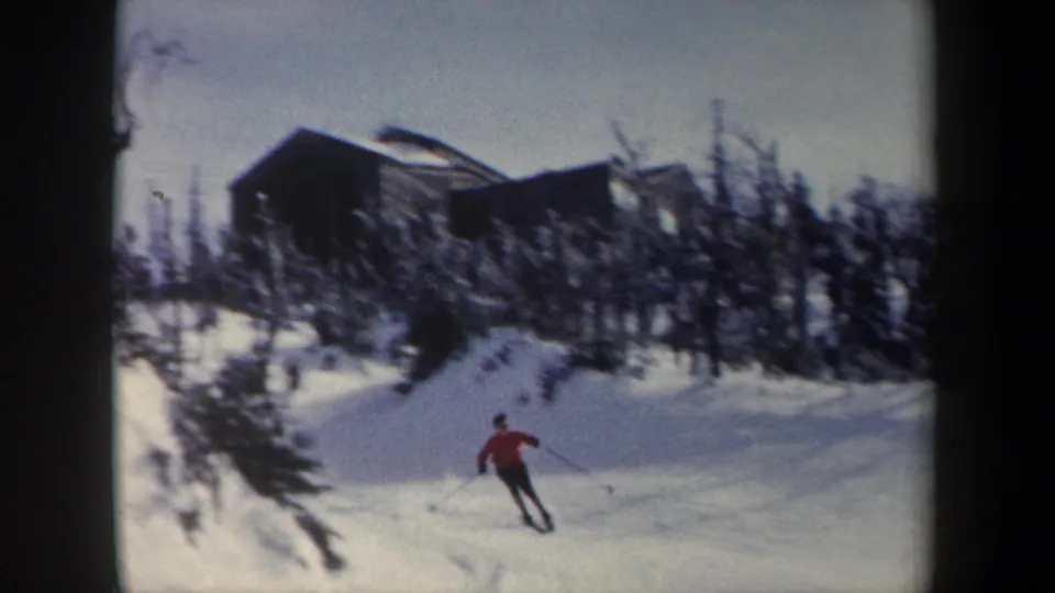Distant skier in a red jacket glides across a snowy 1962 New York slope with bare trees and a cabin-like structure behind.