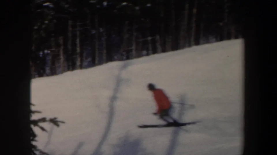 Wide 8mm frame showing the skier farther away on a New York snow slope with dark trees lining the background.