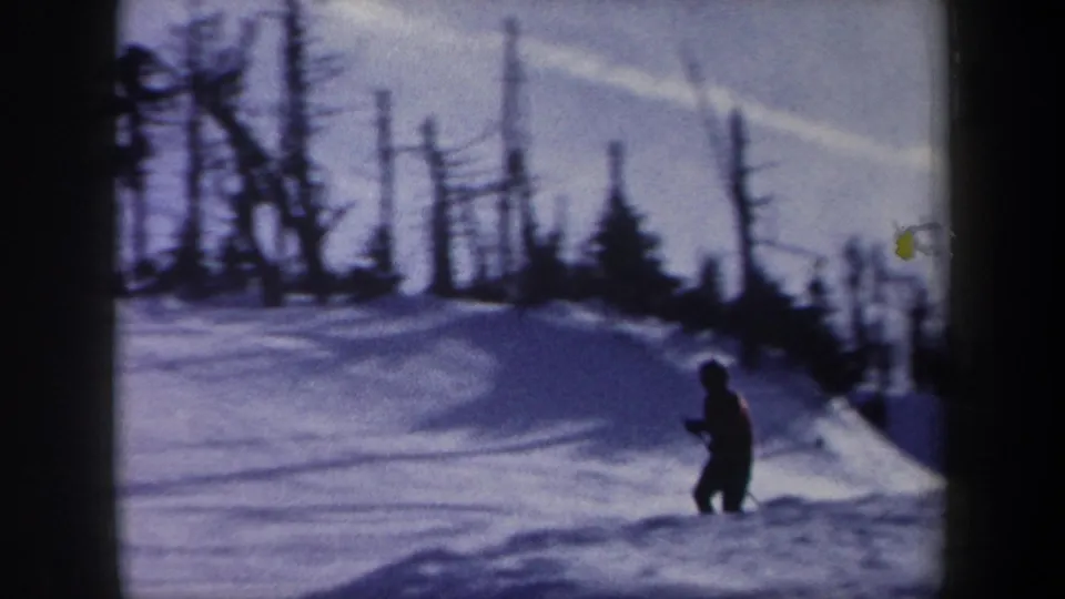 A distant skier is visible on a snowy New York slope beneath bare winter trees in 1962 footage.