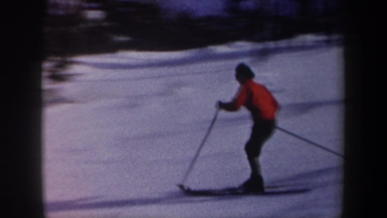 1962 New York home-movie frame showing a skier in a red sweater and dark pants moving across a snowy slope with trees beyond.