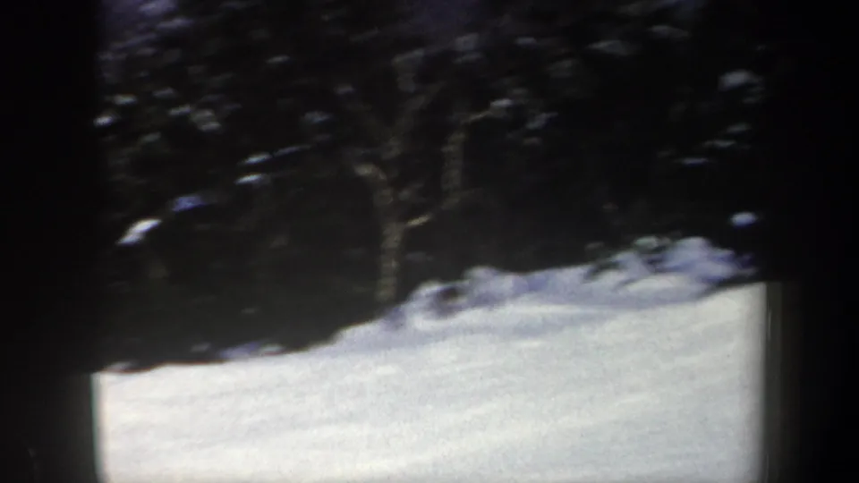 A 1962 New York home-movie frame shows the snowy slope and surrounding dark trees as the skier moves largely outside the visible area.