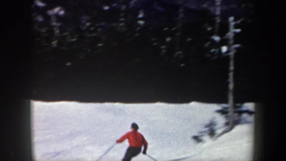 1962 New York 8mm frame with the skier in a red sweater partly low in frame, continuing downhill beside a wooded snowy run.