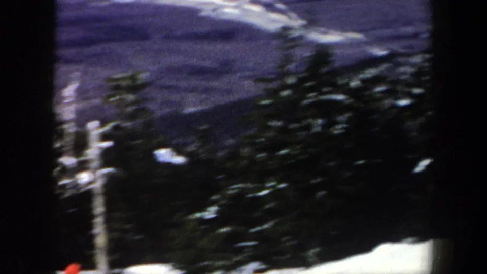 1962 New York 8mm frame with a snowy ski area view, evergreen trees, a pole, and distant ridgeline.