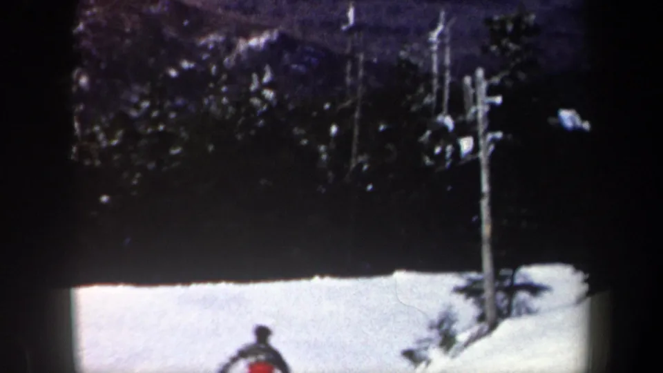 1962 New York 8mm frame showing evergreen trees, a vertical pole, and a bright snowy slope below.