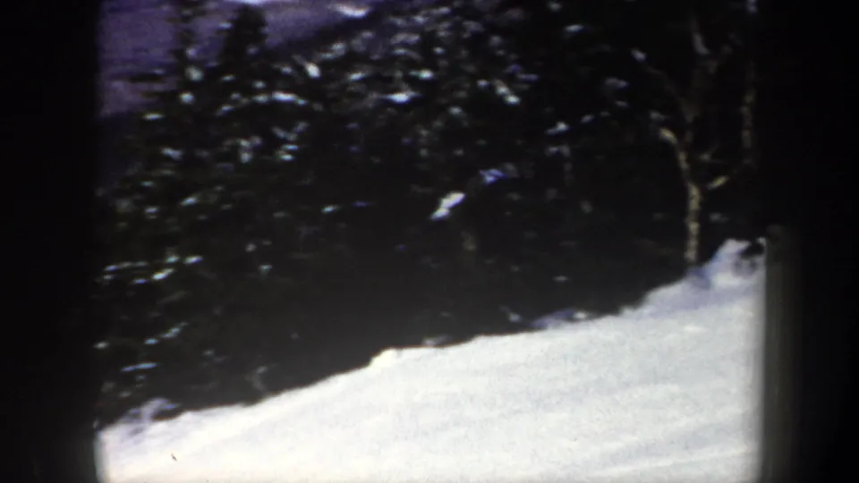 A snow-covered hillside in New York, 1962, framed by dark evergreen trees and rounded 8mm film borders.