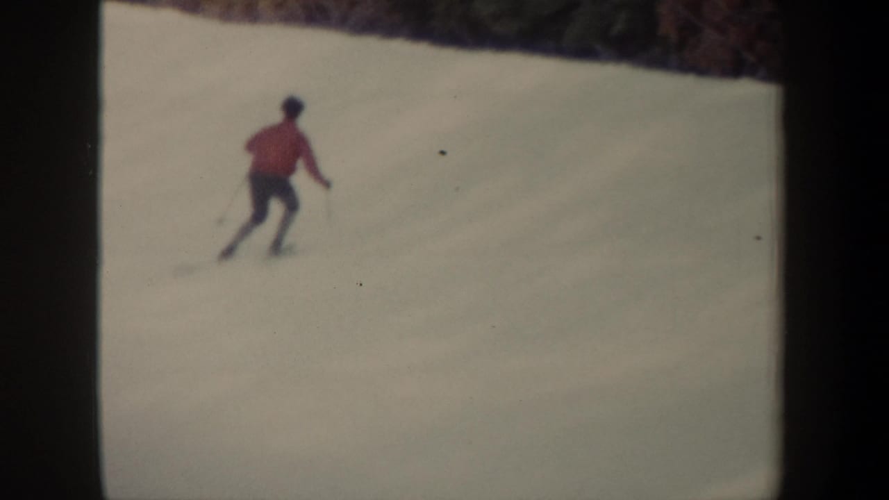 Distant skier in a red jacket gliding across a snowy slope.