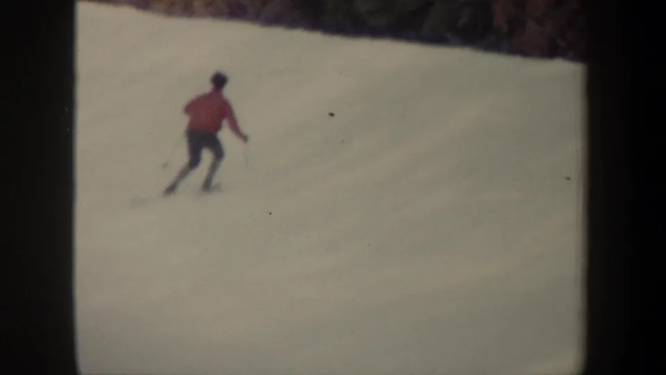 A distant skier in a red jacket and dark pants moves across a snowy New York slope in 1962 home-movie footage.