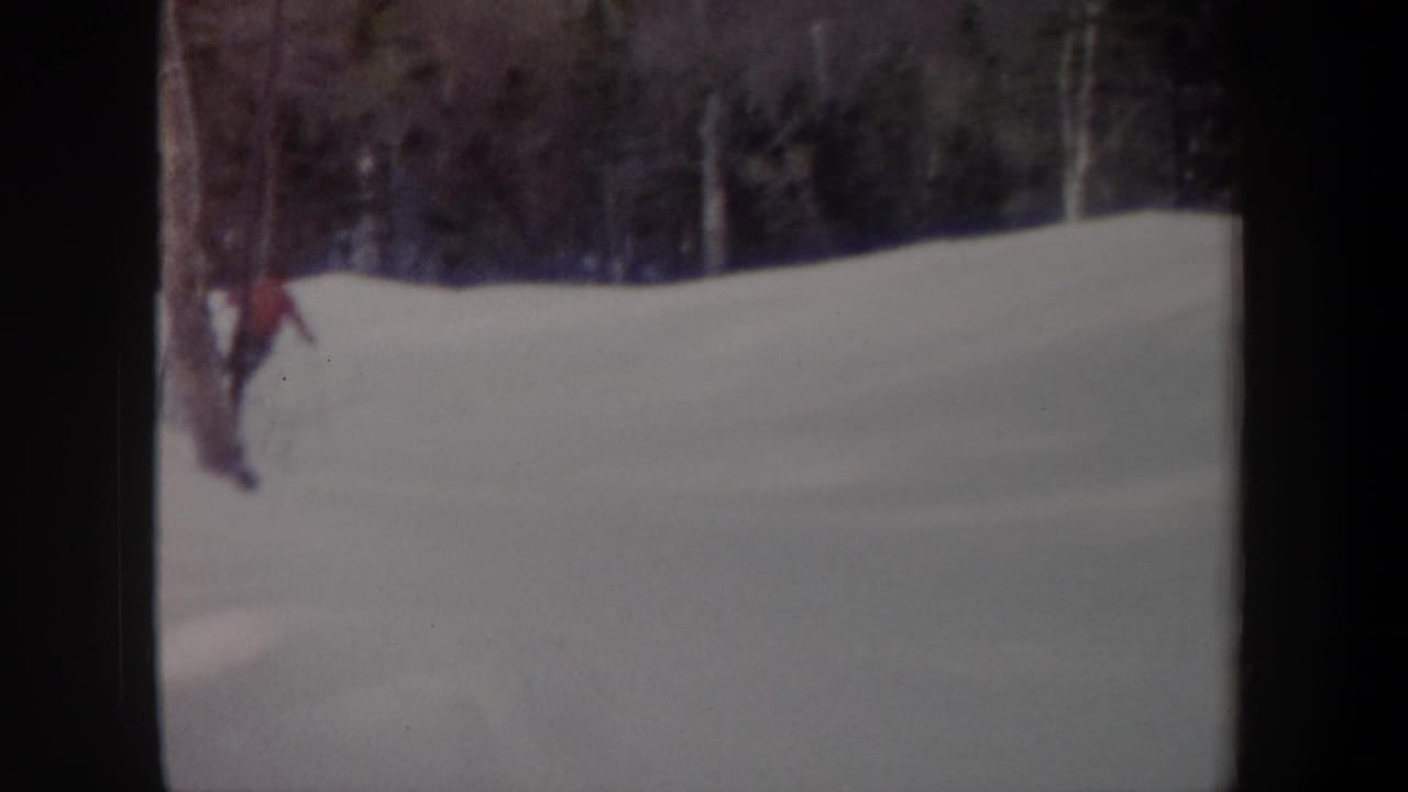A red-clad skier moves downhill through snowy woods with dark film borders.