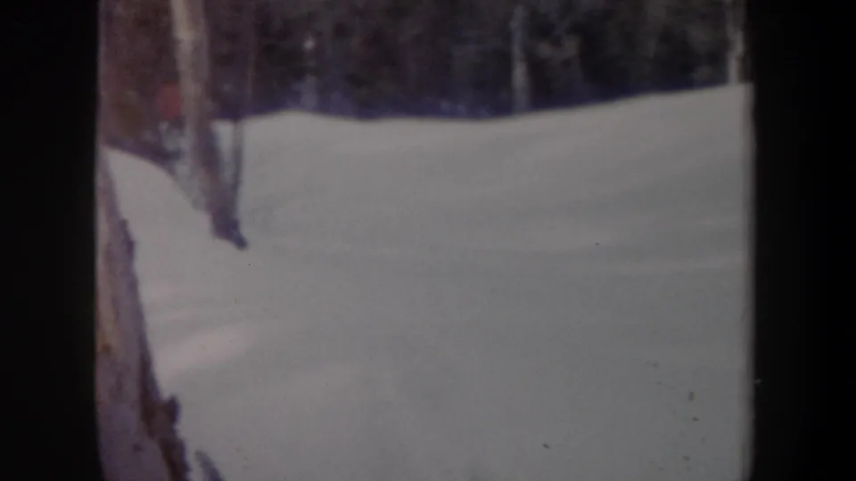 1962 New York 8mm frame with a skier partly obscured by trees on a snowy wooded hillside.