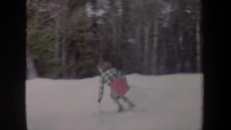 1962 New York 8mm frame showing a plaid-shirted skier with a red pack skiing through snowy woods.