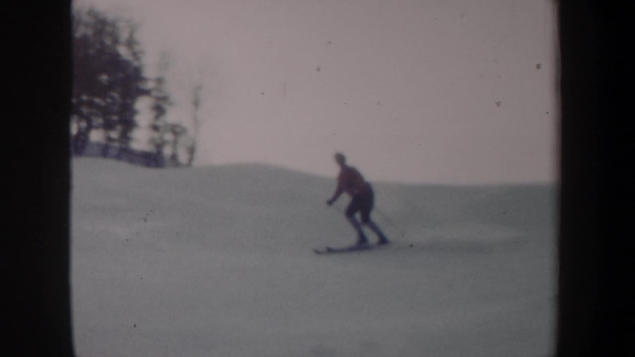 1962 New York 8mm frame showing a distant skier in a red jacket moving downhill across an open snowy slope.