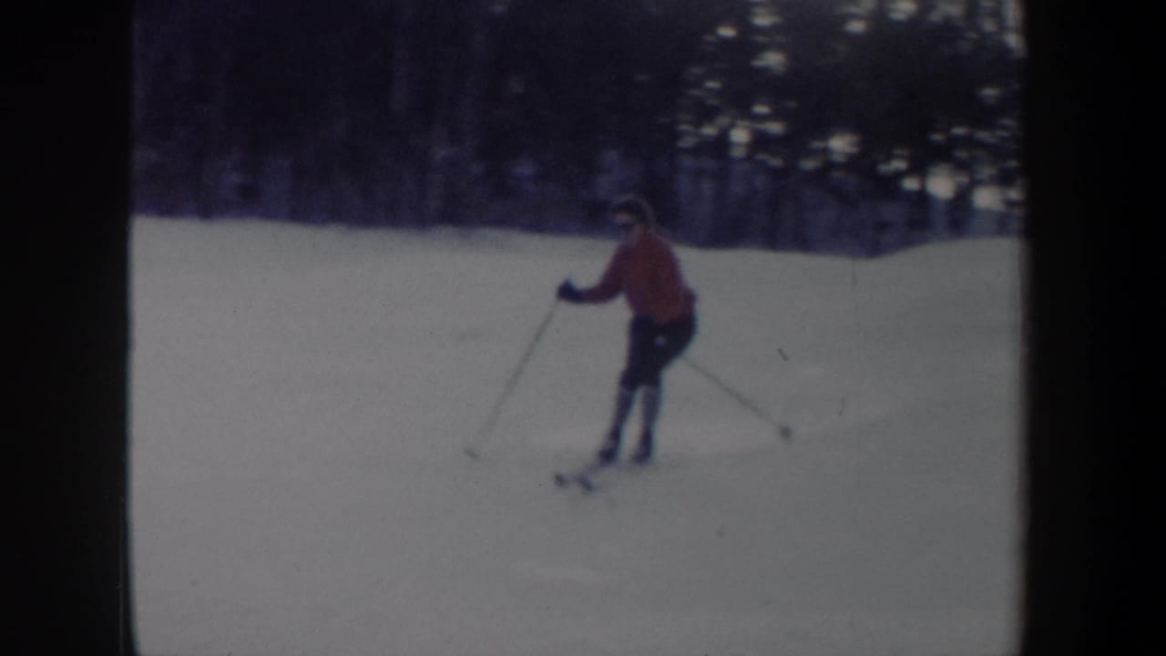 1962 New York home-movie frame of a skier in red moving across a snowy run with poles visible.