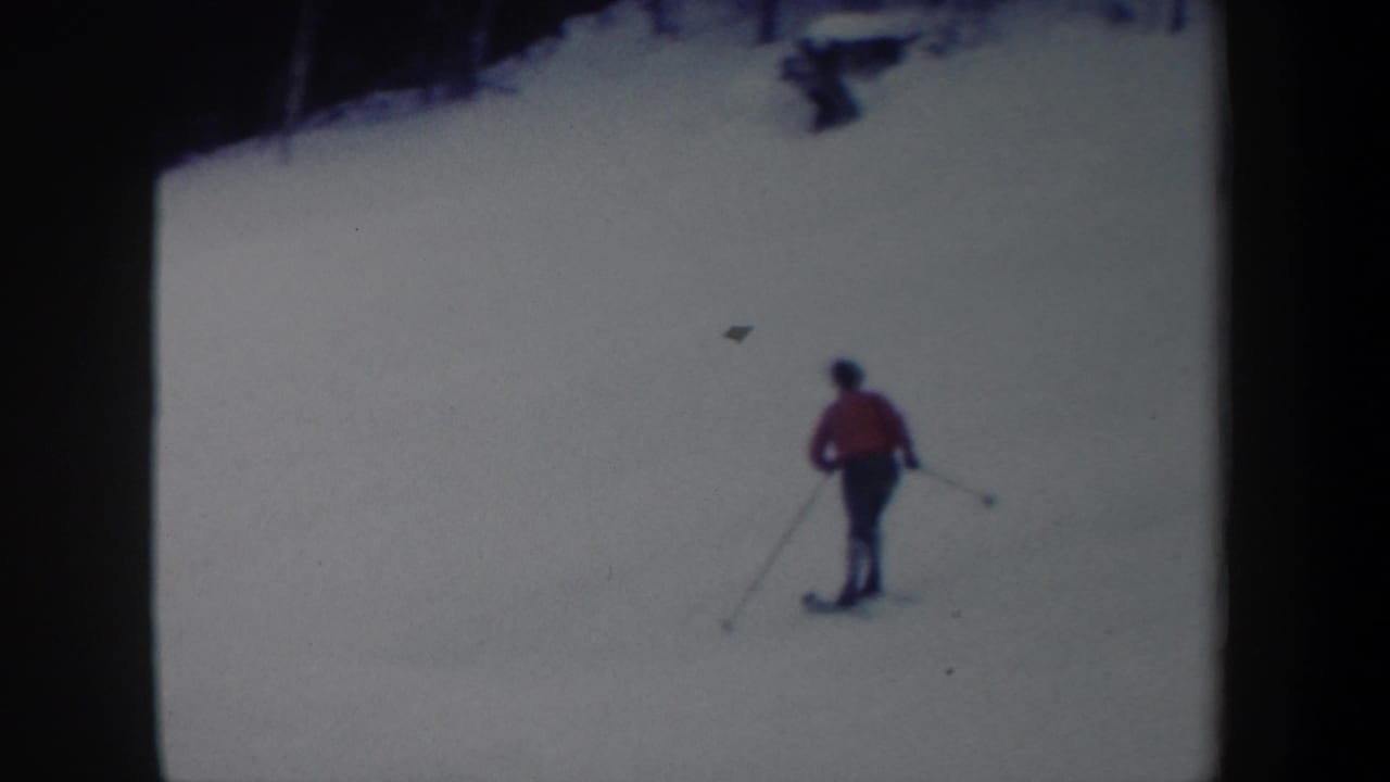 1962 New York 8mm frame showing a distant skier in a red jacket with poles on a bright snowy slope.