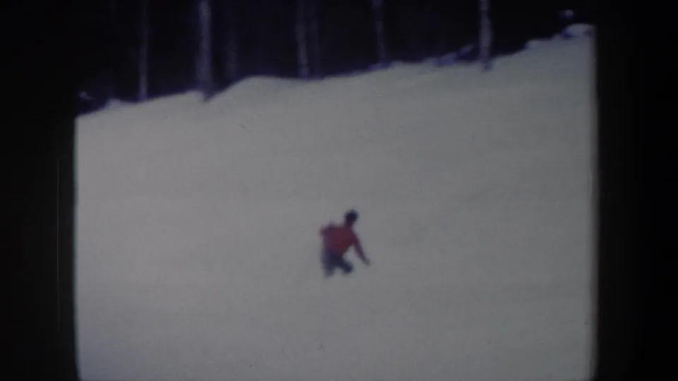 A red-jacketed skier continues down the snowy New York slope in a soft, cool-toned 8mm frame from 1962.