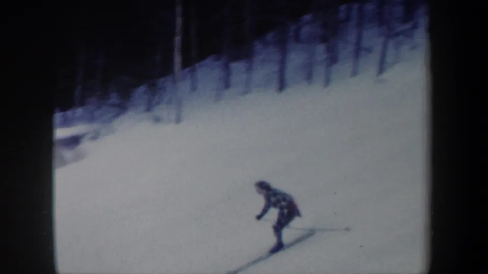 1962 New York 8mm frame showing a woman leaning into a downhill ski run on a wide snowy slope.