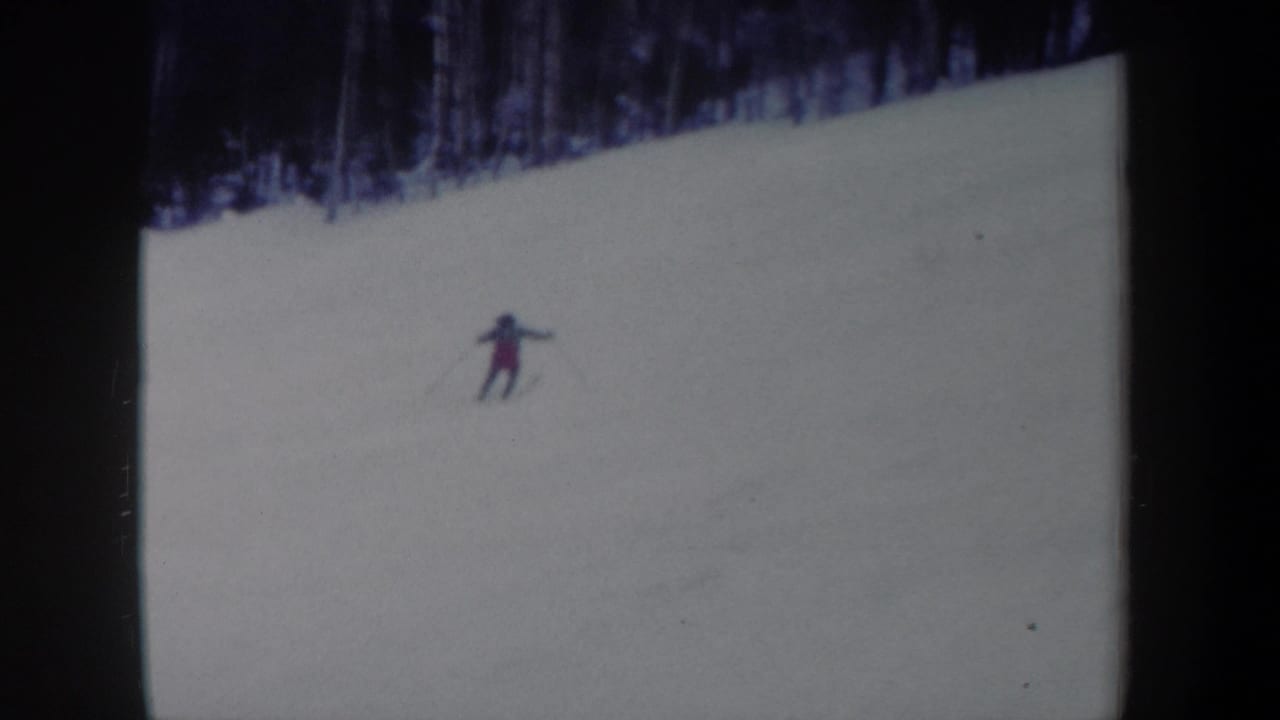 Distant skier in 1962 New York 8mm footage traversing a snow-covered hillside below bare trees.