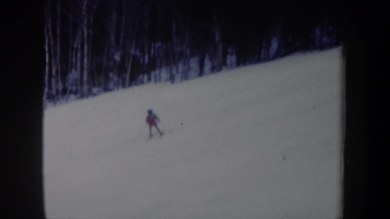 A lone skier continues across the snowy New York hillside, small in frame against the open slope.