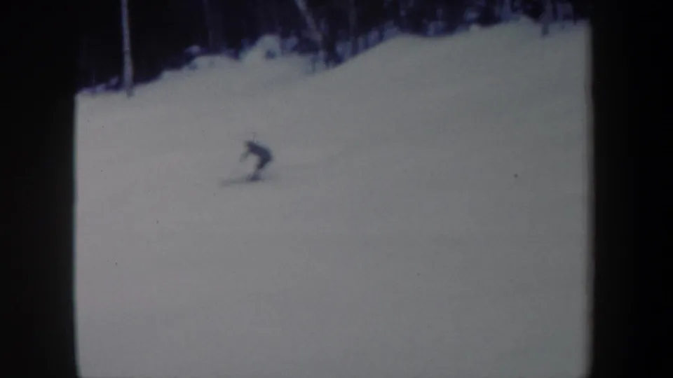 A distant skier leans or crouches on the snow-covered New York hillside near the end of the 8mm clip.