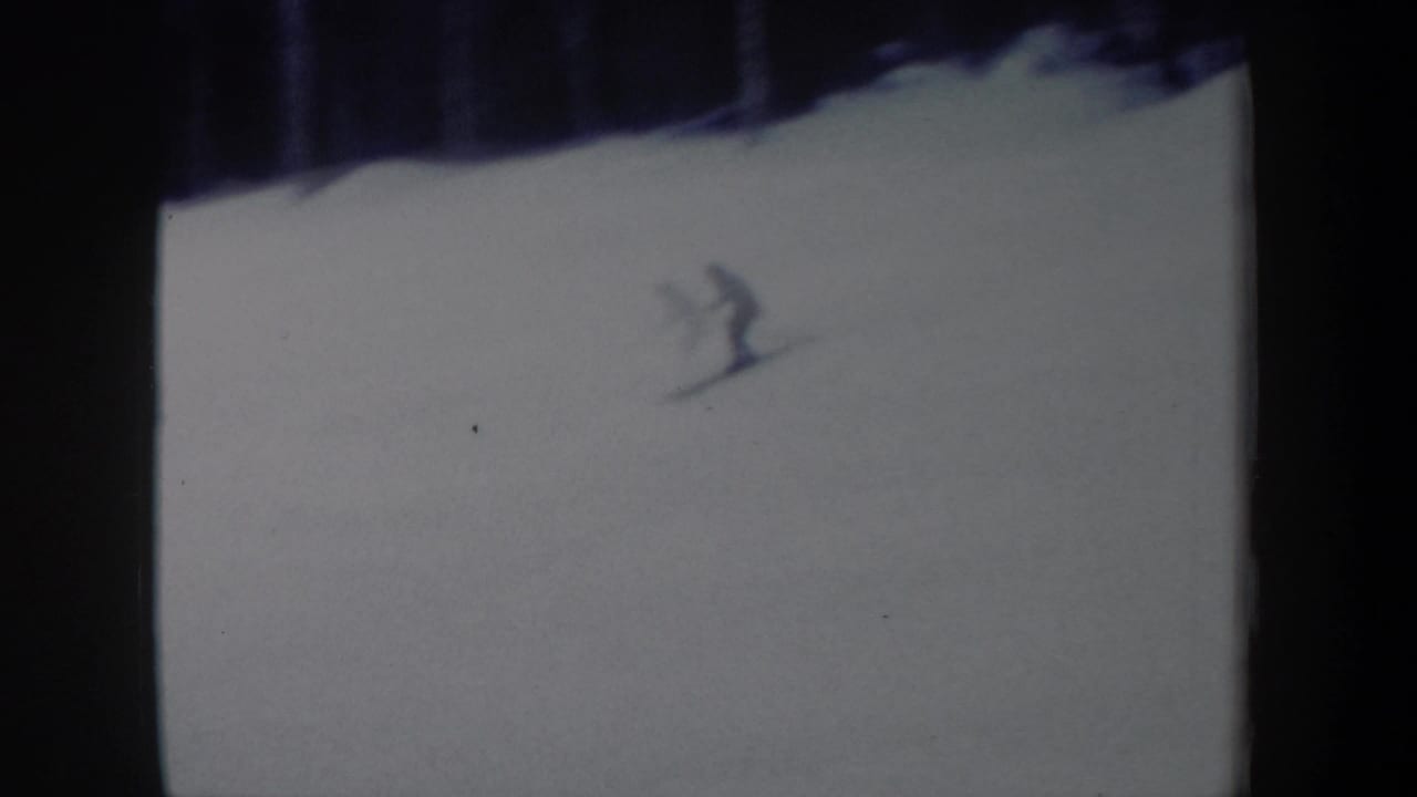 1962 New York 8mm frame showing a distant skier on a broad white slope below a dark tree line.