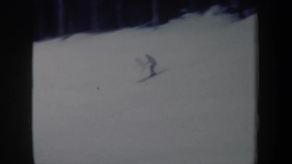 1962 New York 8mm frame showing a distant skier on a broad white slope below a dark tree line.