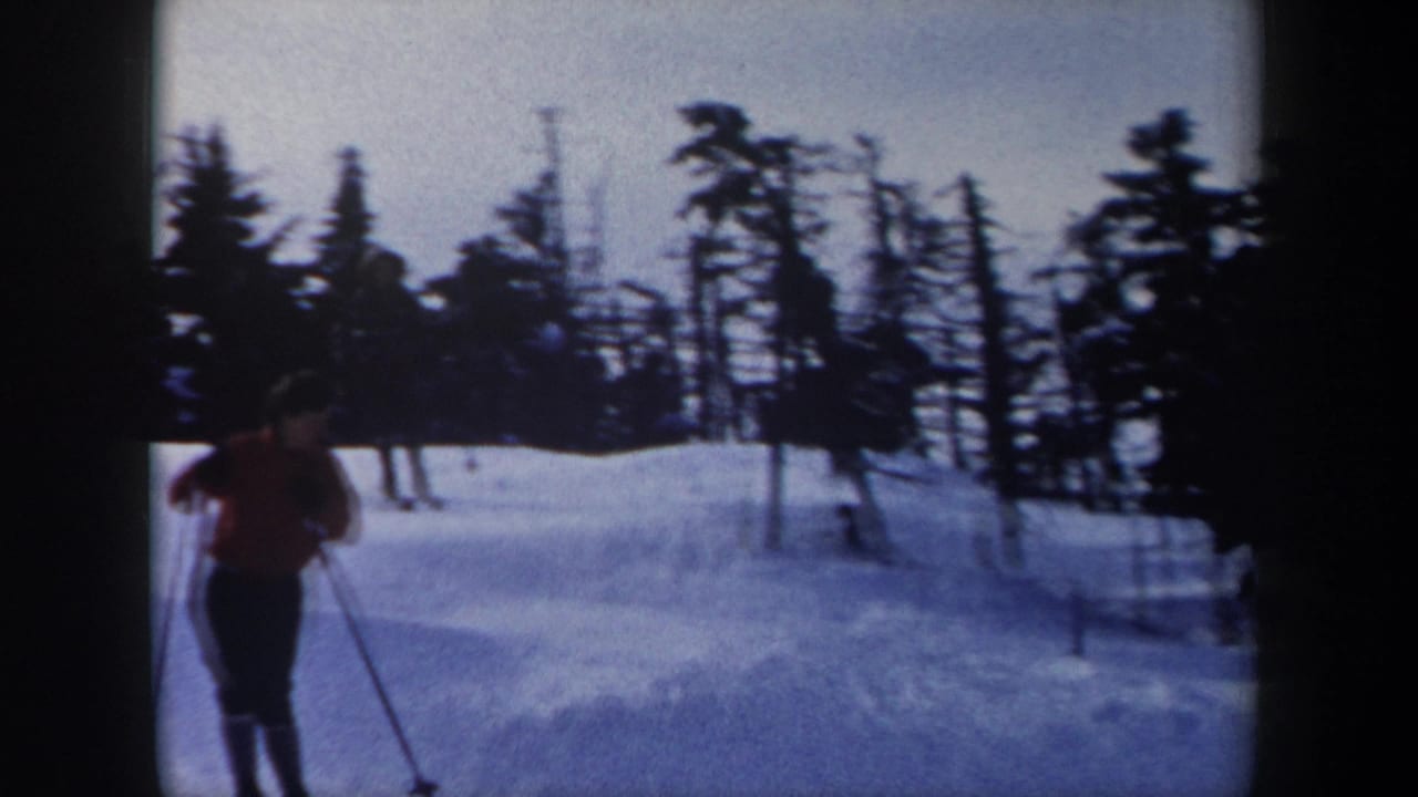 1962 New York 8mm frame showing a skier in a red jacket descending a snow-covered slope bordered by dark trees.