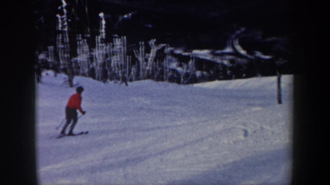 1962 New York 8mm frame showing a skier in a red jacket moving across a snow-covered wooded slope.