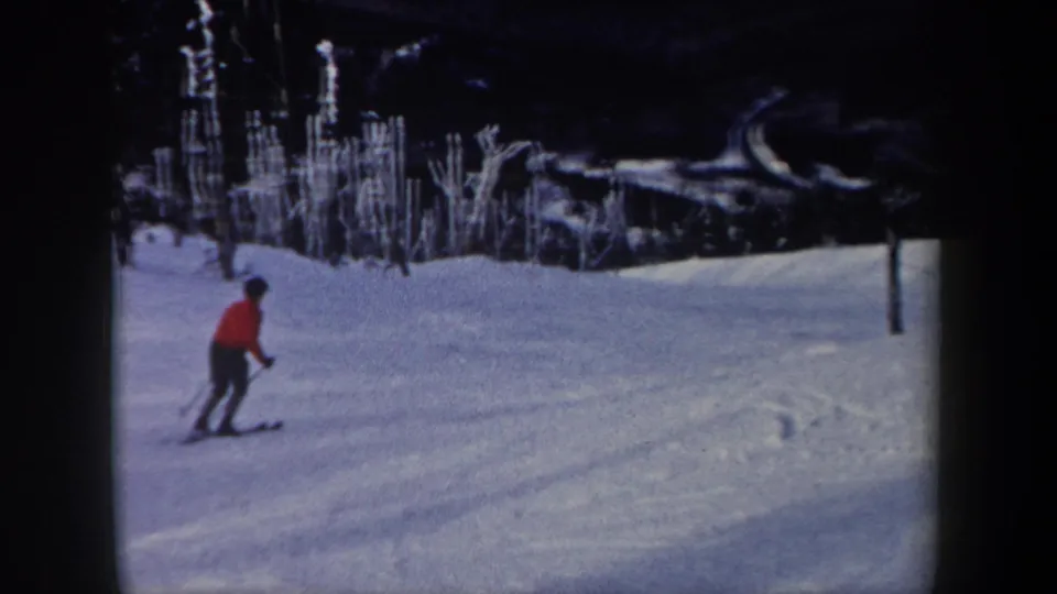 1962 New York 8mm frame showing a skier in a red jacket moving across a snow-covered wooded slope.