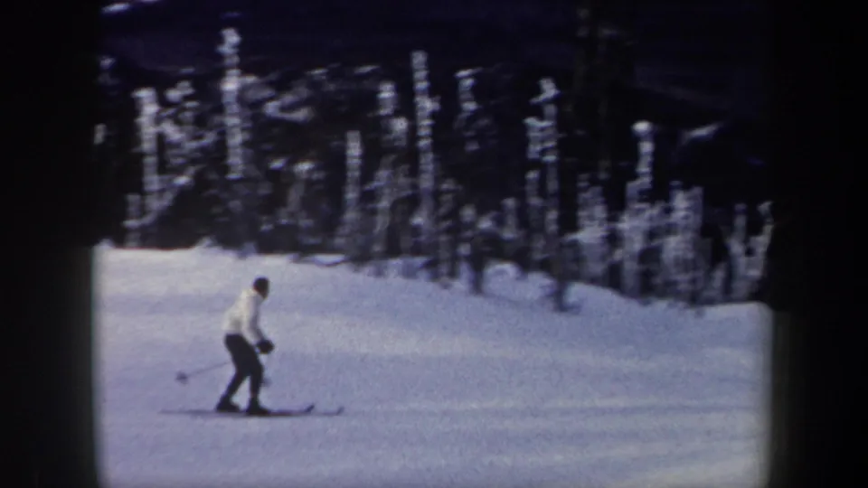 1962 New York 8mm frame showing a distant skier gliding across a snowy forest slope with ski poles.