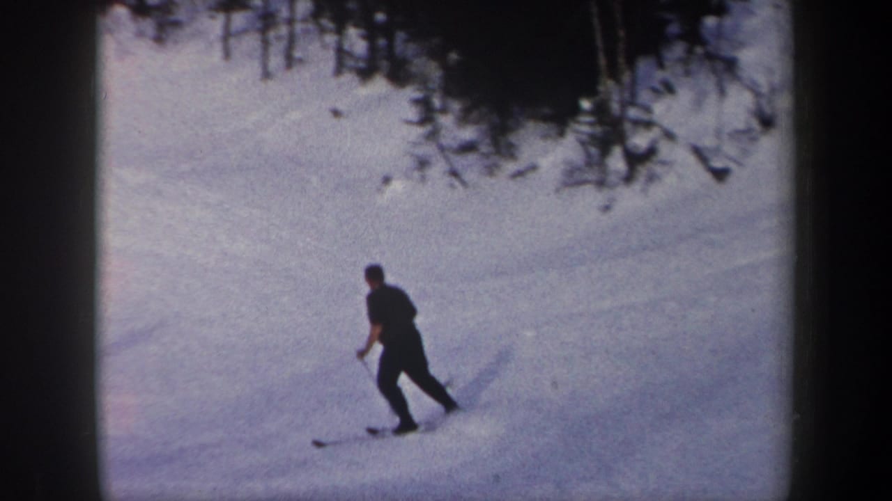 A skier in dark clothing crosses a bright snowy slope with poles.
