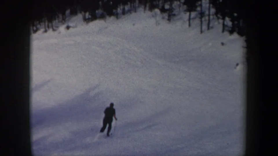 1962 New York 8mm frame showing a distant skier on a wide snowy mountain slope below a dark line of trees.