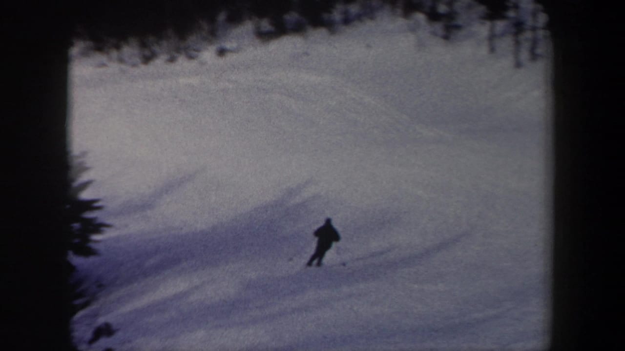 A lone skier in dark winter clothing moves across a snowy New York slope in 1962 home-movie footage.