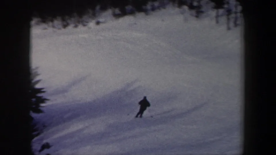 A lone skier in dark winter clothing moves across a snowy New York slope in 1962 home-movie footage.