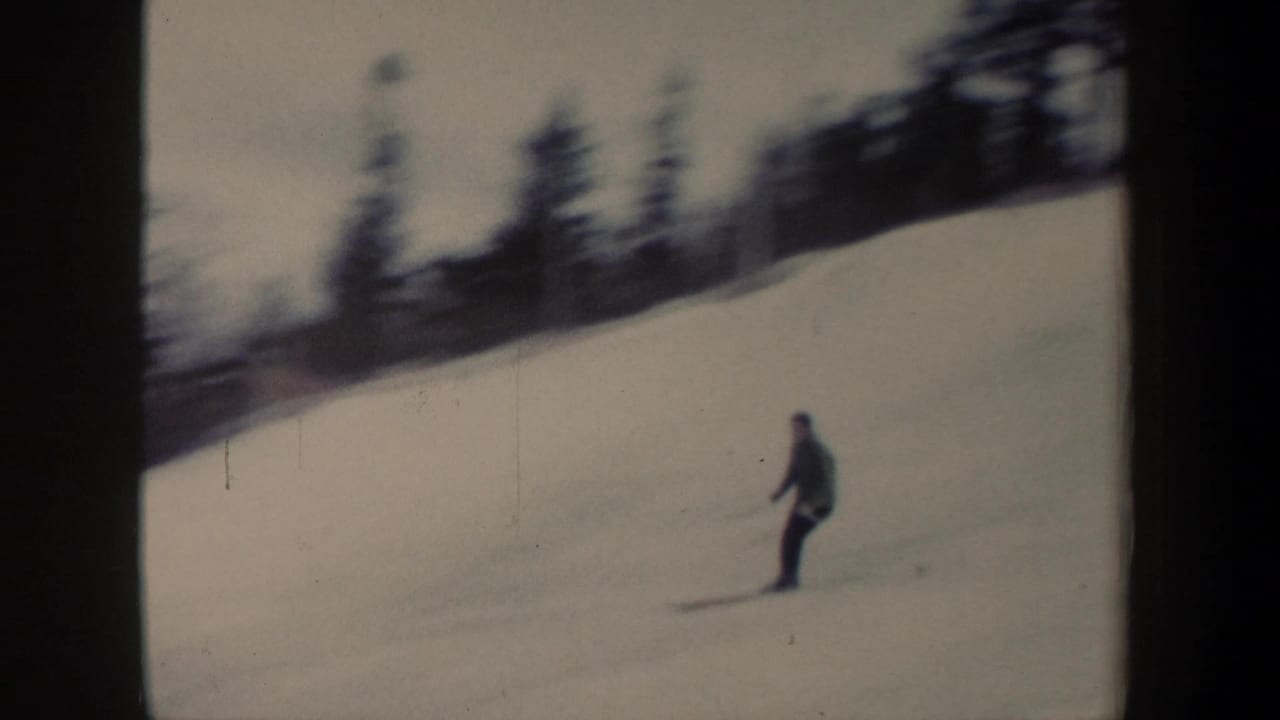 1962 New York 8mm frame showing a lone skier in dark clothing moving down a snowy slope below a tree line.